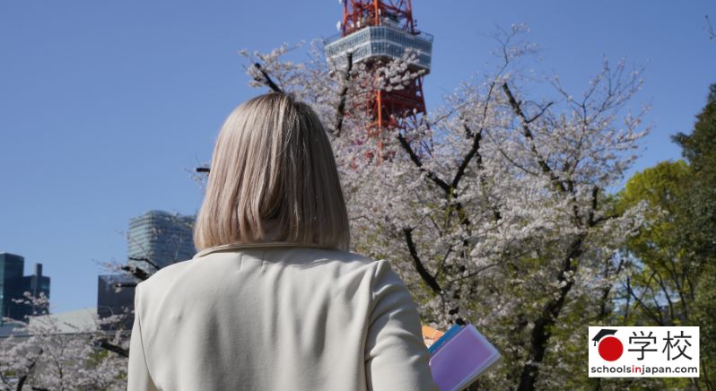 Student from behind standing near tokyo tower and cherry blossom trees, trying to choose a university in Japan.